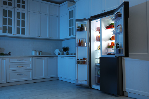 Refrigerador abierto lleno de comida en la cocina por la noche photo