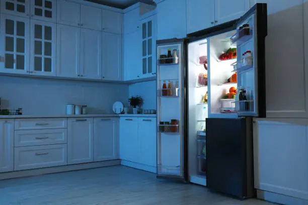 Photo of Open refrigerator filled with food in kitchen at night