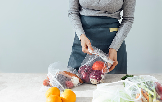 Unrecognizable woman putting fresh fruit and vegetables in reusable bag at home