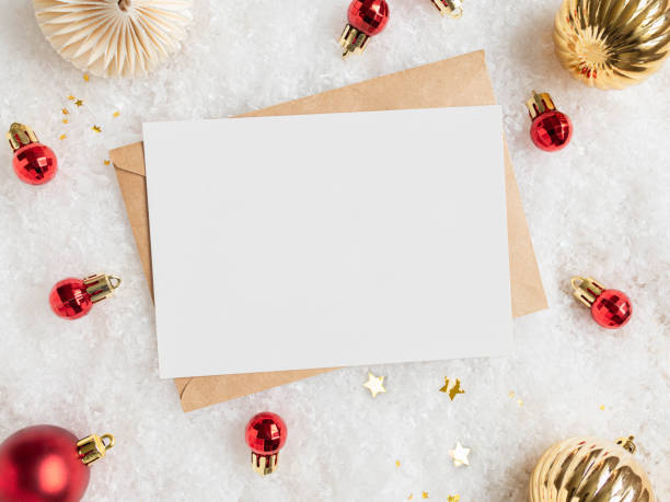 Empty white postcard and craft envelope and various christmas decor on artificial snow background