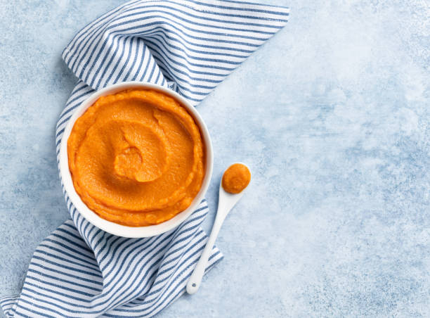 Pumpkin puree (mashed butternut squash) in white ceramic bowl top view. Copy space. Seasonal cooking concept. Blue and white stripes textile, white tea spoon. Ingredient for autumn baking. mashed stock pictures, royalty-free photos & images