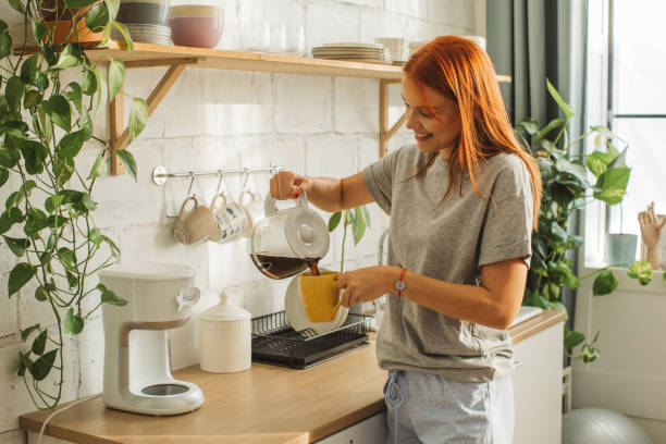 College student at dorm room Young woman at dorm room. It is morning and she is making  first coffee while checking smart phone. coffee maker stock pictures, royalty-free photos & images