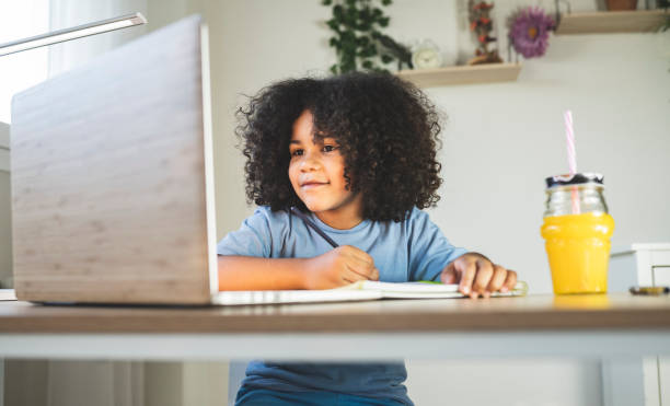 istock pretty curly-haired boy, does his homework at home with a bamboo computer, house with plants, eco 1336092060