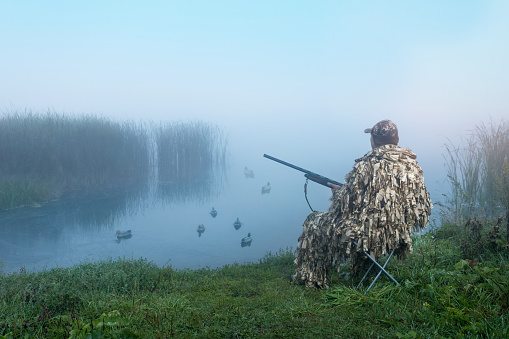 Waterfowl Hunter With Gun. A Hunter In Camouflage Hunting On Ducks In Summer Or Autumn Season.
