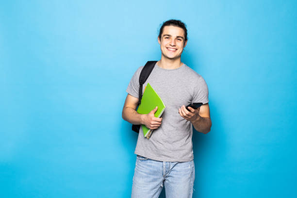 istock Young handsome man with backpack, headphones and cup of coffee on blue background 1336098521