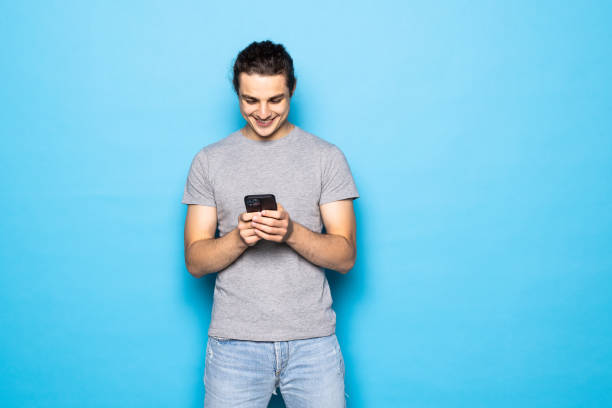 istock Excited young man posing isolated over blue wall background using mobile phone chatting. 1336100101