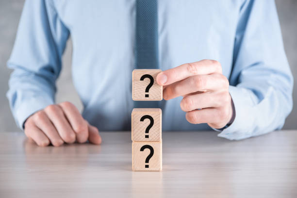 istock Businessman hold and put wooden cube block shape with question marks on grey table. Space for text.concept for confusion, question or solution 1336100962