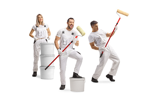Group of cheerful house painters dancing and playing with paint rollers isolated on white background