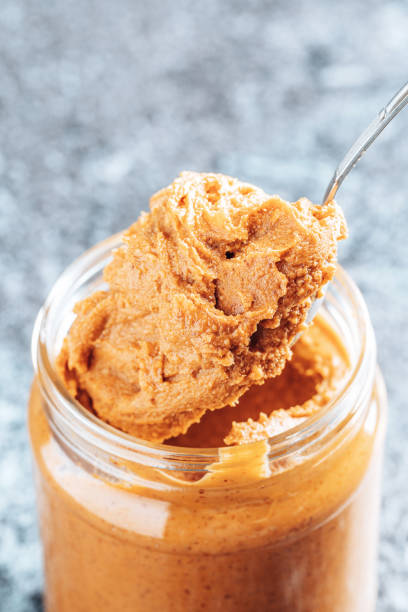 istock Spoon dipping into a glass jar with crunchy peanut butter. 1336103360
