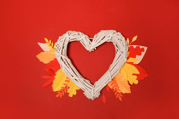 Autumn heart symbol with orange falling leaves on red background