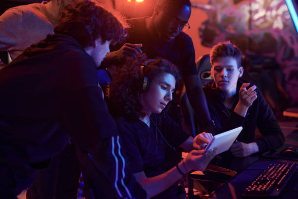 istock Young curly-haired man in headphones using tablet while explaining strategy of online game to friends in computer club 1336104181