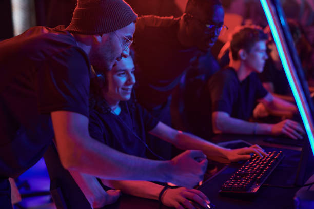 istock Multi-ethnic gamers standing at computer and overseeing how young guy playing video game in esports bar with neon illumination 1336104212