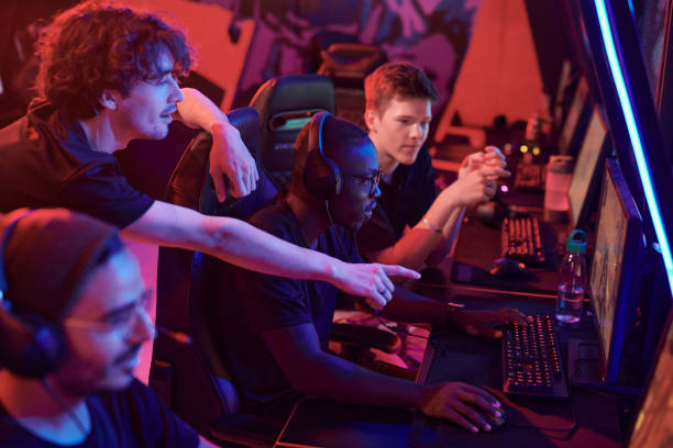 istock Young man pointing at computer screen while giving advice to African-American gamer focused on game in esports club 1336104297