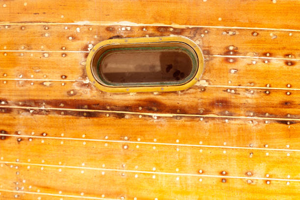 boat oval aged brass porthole in wooden hull with caulking putty and screw