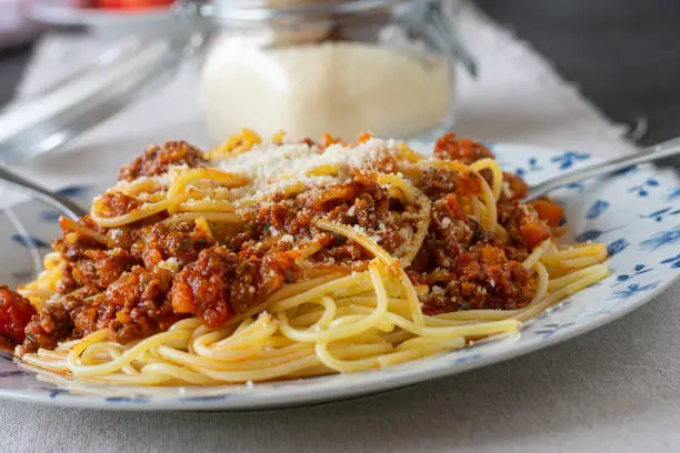 Traditional and homemade cooked spaghetti with bolognese sauce served on a rustic plate with grated parmesan cheese. Closeup and front view