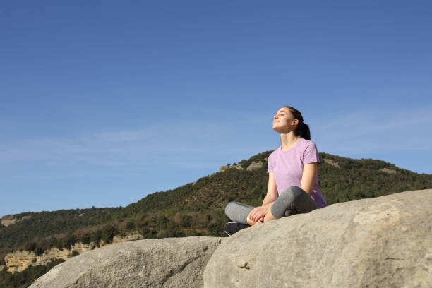 sportlerin entspannt sich auf einer klippe aus - zen like nature breathing exercise sitting stock-fotos und bilder