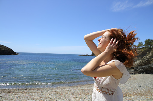 Happy woman touching hair in a windy beach day