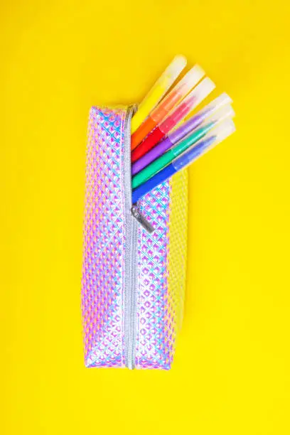Fashionable holographic pencil case with multicolored felt-tip pens or markers on bright yellow background. Back to school.