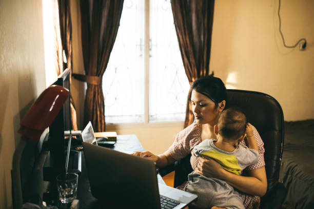 madre che tiene il suo bambino quando si lavora da casa - laptop adult curtain business foto e immagini stock