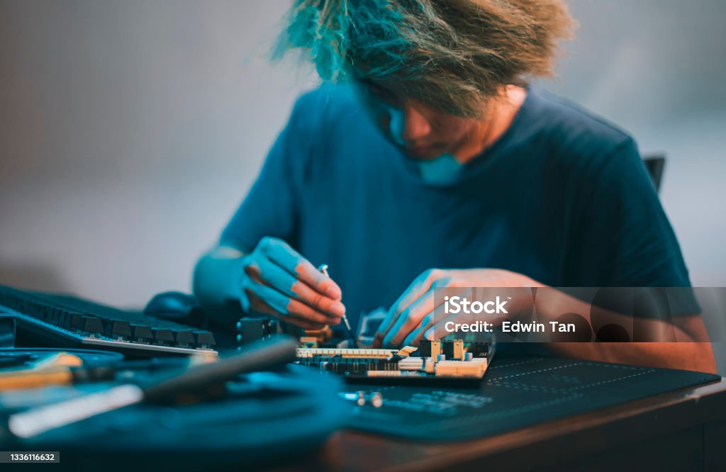 asian chinese teenage boy repairing computer motherboard with work tool diagnosis tighten at night at home Teenager Stock Photo