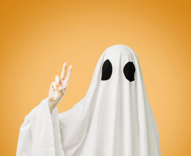 istock Halloween white ghost showing peace sign gesture on yellow background. 1336124156