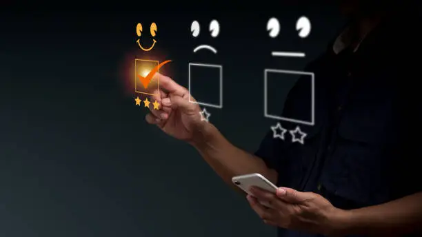 Photo of A man uses a finger to point and chooses a face smile emoticon to show on the virtual screen. The survey, poll, or questionnaire for user experience or customer satisfaction research.