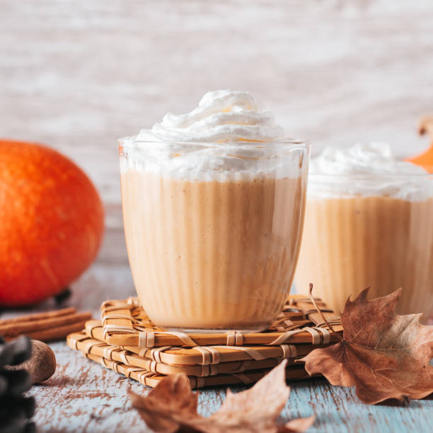 latte de citrouille sur table en bois usée avec des cônes de cèdre et des feuilles sèches. nature morte d’automne avec smoothie à la citrouille décoré de gros plan à la crème fouettée - latté pumpkin spice coffee photos et images de collection