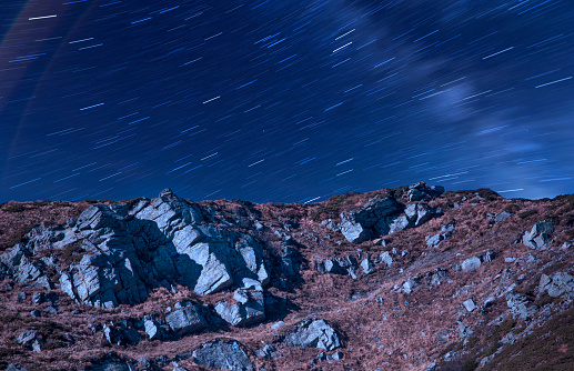 A rocky mountain slope, and a defocused night starry sky with a milky way. Wonderful night mountain landscape.
