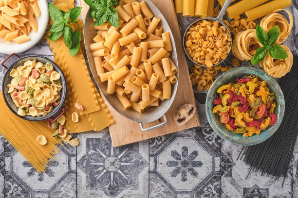 pasta. italian pasta. variety of traditional italian pasta: colorful spaghetti, tagliatelle, farfalle, penne, ptititm, noodle, fusilli, cannelloni on an old stone background. top view with copy space. - cooking oil olive oil nutritional supplement spoon imagens e fotografias de stock