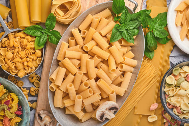 pasta. pasta italiana. varietà di pasta tradizionale italiana: spaghetti colorati, tagliatelle, farfalle, penne, ptititm, noodle, fusilli, cannelloni su un vecchio sfondo di pietra. vista dall'alto con spazio di copia. - cooking oil olive oil nutritional supplement spoon foto e immagini stock