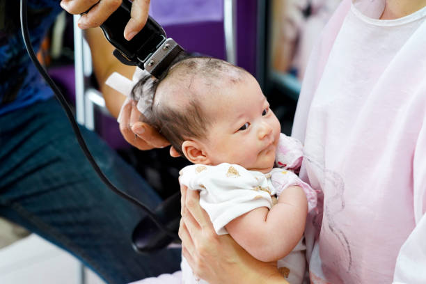 bébé d’un mois est rasé les cheveux, c’est traditionnel thaïlandais doit faire raser les premiers cheveux dès la naissance. mère tenant bébé assis sur ses genoux dans le barbier. - baby yawning asian ethnicity newborn photos et images de collection