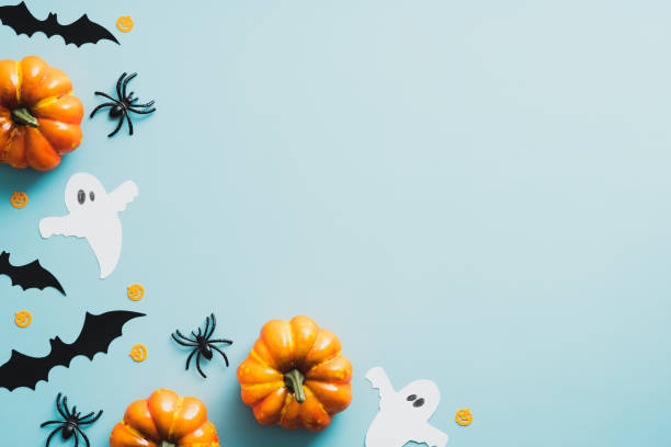 istock Happy halloween flat lay composition with ghosts, bats, spiders, orange pumpkins on blue background. Top view with copy space. 1336139684