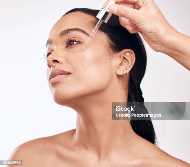 Shot Of A Beautiful Young Woman Posing With A Serum Dropper Against Her Face Stock Photo - Download Image Now