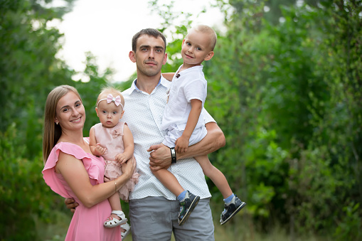 Husband and wife and their little children. Family portrait in nature. Mom and Dad are posing with their brother and sister. Young family with children for a walk in the woods.