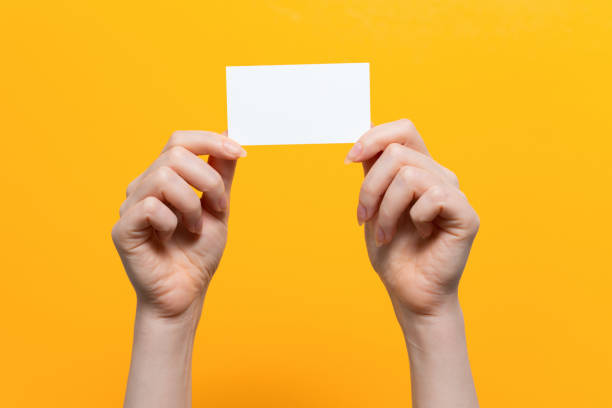 istock Woman's hands hold a white card. Close up. Yellow background. Mock up 1336153516