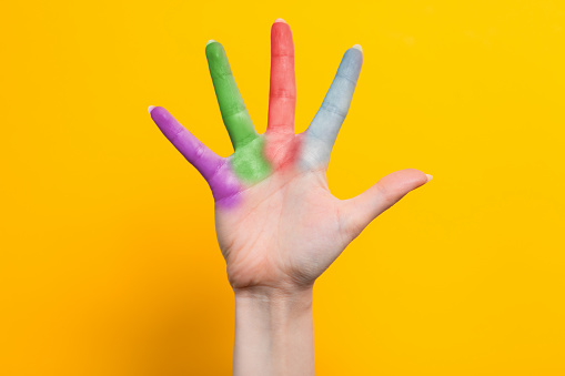A woman's hand with multicolored fingers spread out. Yellow background. The concept of the world day of protection of children.