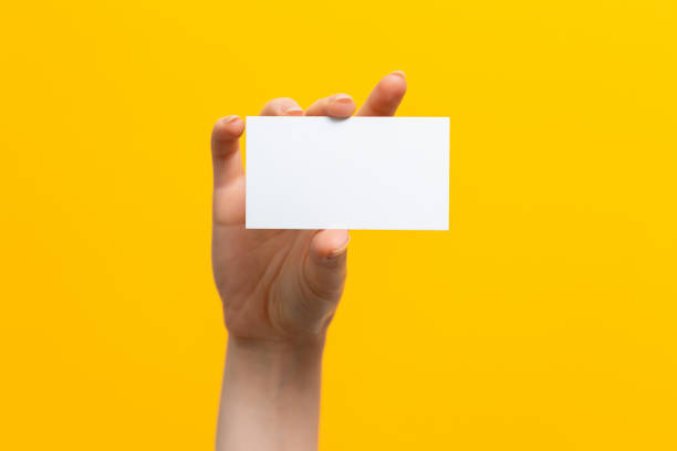 istock Raised female hand holding a white card. Mock up. Yellow background. Copy space 1336153525