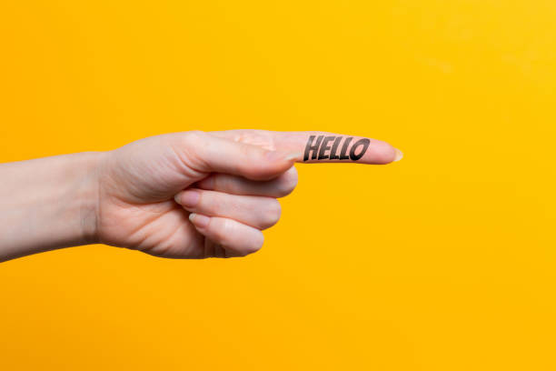 istock Female hand close-up, index finger pointing at something with text Hello. Gesture of direction. Yellow background. Copy space 1336153531