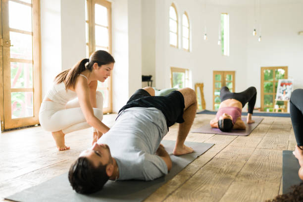 Caucasian woman teaching how to do a yoga pose Let me help you. Beautiful yoga instructor helping a young man to maintain a bridge pose during group class yoga instructor stock pictures, royalty-free photos & images