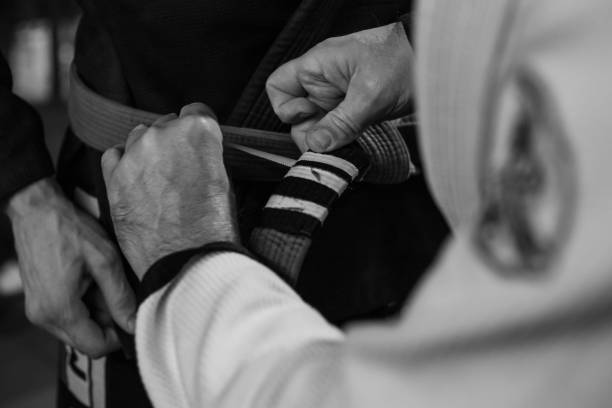 Promotion during brazilian jiu jitsu training. Close up, black and white photo of trainer's hand adding third white stripe to adept's belt. Photoshoot from training of one of Jiu-Jitsu clubs in Poznan, Poland. judo photos stock pictures, royalty-free photos & images