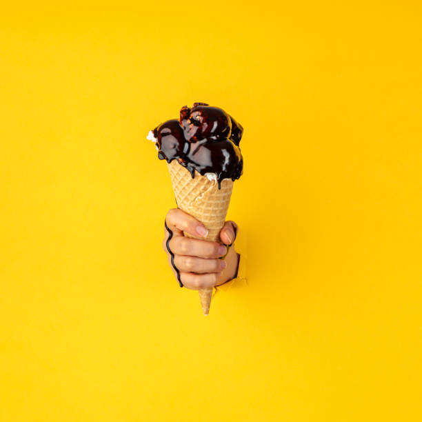 istock Through yellow torn paper female hand holding ice cream with chocolate 1336159704