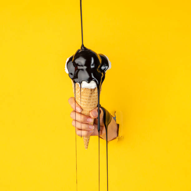 Through yellow torn paper female hand holding ice cream with chocolate