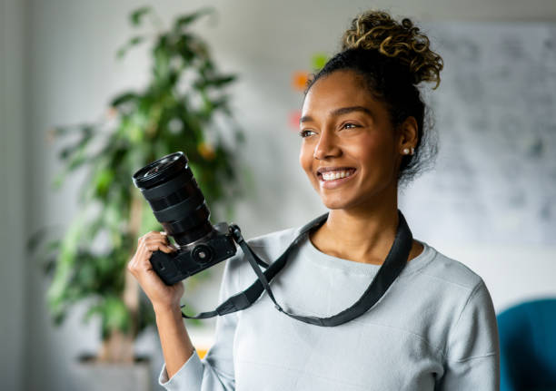 Freelance female photographer holding a camera Portrait of an African American freelance female photographer holding a camera and smiling - creative occupation concepts photographer stock pictures, royalty-free photos & images