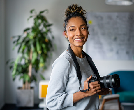 Portrait of a happy African American photographer holding a camera and smiling at the office - creative occupation concepts