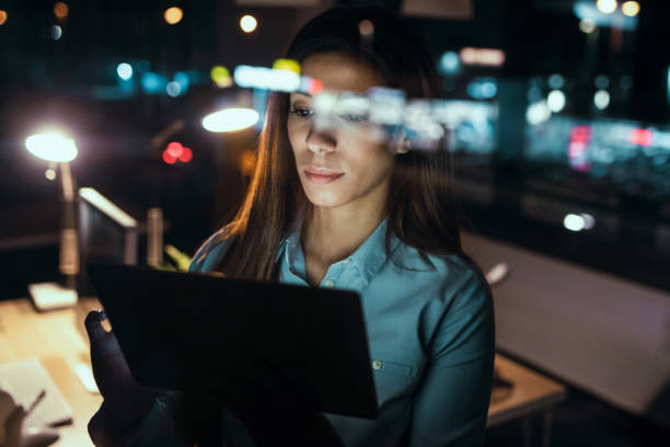 istock Smart pretty business woman taking a break while cheaking her digital tablet standing in the office at night. 1336166893
