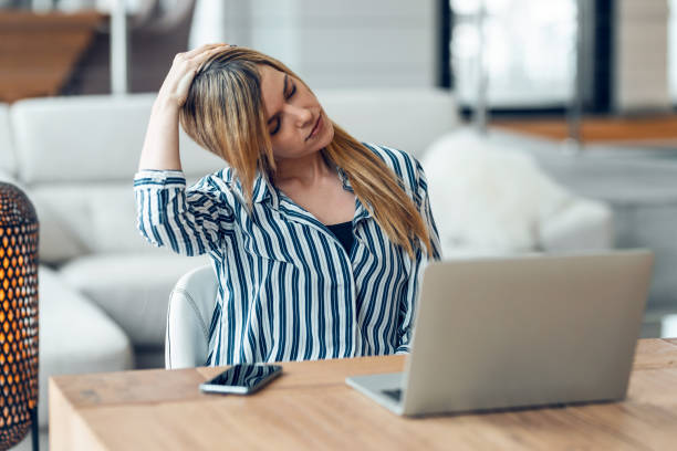 istock Tired business woman with neck pain looking uncomfortable while working with computer in living room at home. 1336169346