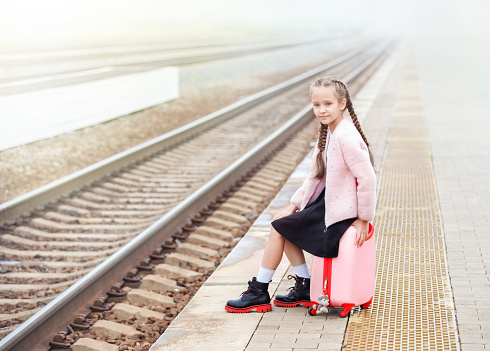 a girl with a pink suitcase is waiting for a train on the station platform