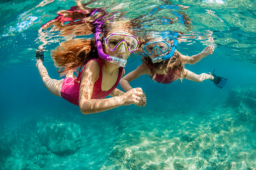 Two girls in pink swimsuits enjoy playing underwater and snorkeling in the crystal clear water of the Adriatic sea during their cool summer vacation.