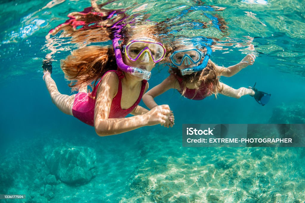 Sisters snorkeling and playing underwater Two girls in pink swimsuits enjoy playing underwater and snorkeling in the crystal clear water of the Adriatic sea during their cool summer vacation. Snorkeling Stock Photo