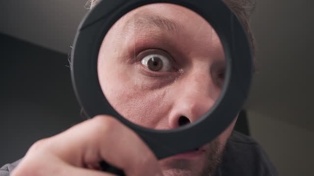 a curious funny surprised Middle-aged  man eye who is looking at the camera through a magnifying glass. Humorous